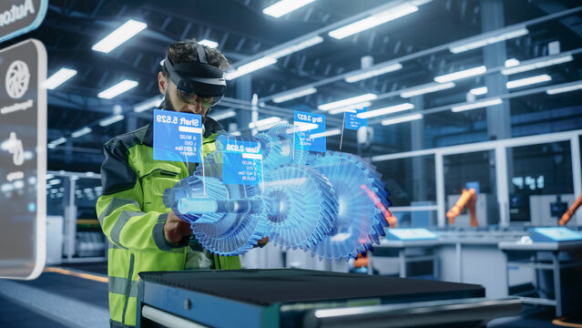 Automotive Factory Engineer Using Augmented Reality Headset in a Modern Facility with Automated Robotic Arms on an Assembly Plant. Specialist Ananlyzing and Manipulating a Virtual Gearbox Model