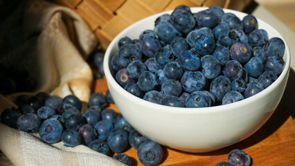A bowl of ripe blueberries sits on a wooden board with a woven basket in the background, creating a rustic and natural setting ideal for showcasing healthy, fresh, and organic food. Close up