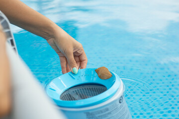 Woman cleaning pool skimmer basket with leaves floating in swimming pool
