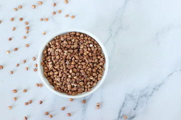 Buckwheat seeds in a bowl on white marble background. Top view. Copy space.