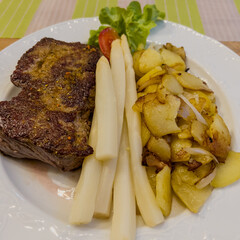 Steak with asparagus and fried potatoes on white plate