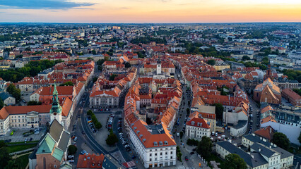 Aerial dusk panorama of Kalisz, view of St. Joseph’s Church, town hall and market square, red rooftops of historic townhouses in city center.