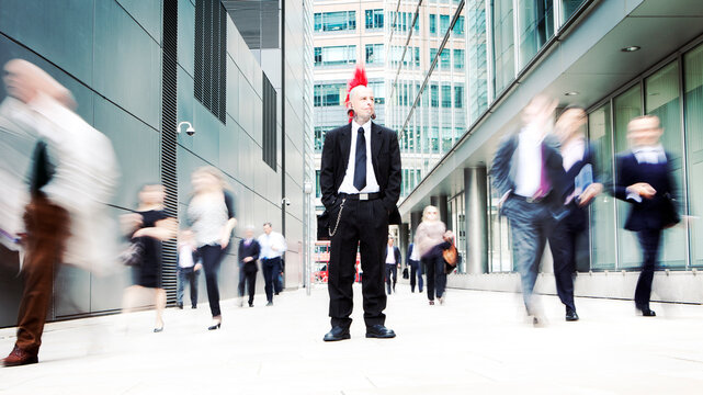 Business Punk. A punk business man standing out from a blurred corporate crowd. His alternative culture contrasts with his environment showing individuality, nonconformity, and independence.