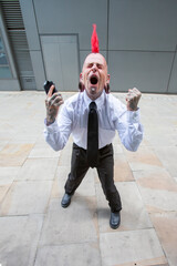 Business Punk. A smartly dressed punk with a red mohawk and tattoos screams in frustration with his...