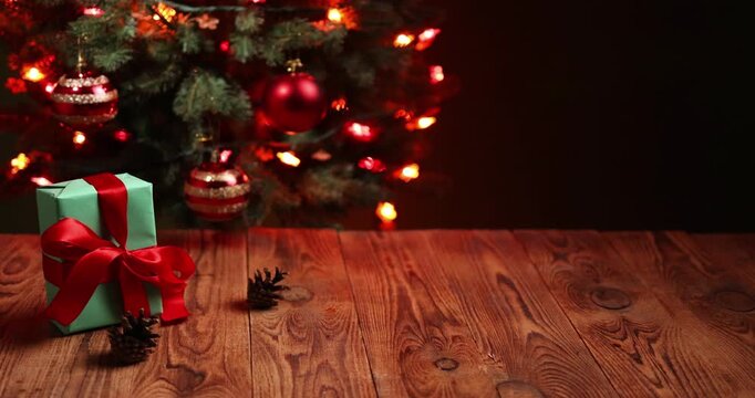 Festive New Year setting shows a wrapped gift and pine cones placed on a wooden surface. Christmas tree lights twinkle in the background, leaving space for text.