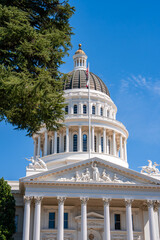 Obraz premium The California State Capitol in Sacramento features a neoclassical dome with a golden sphere, white columns, a U.S. flag, and a bright blue sky.