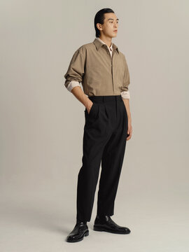 Stylish young man in a brown shirt and black pants standing confidently.