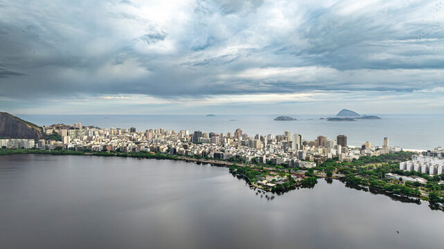 Aerial view of Rio de Janeiro with Lagoa Rodrigo de Freitas, Ipanema beach and Atlantic Ocean islands under dramatic cloudy sky, showing urban skyline and coastline, shot by DJI Mavic 3 drone - Powered by Adobe