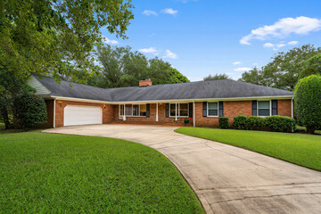 Obraz premium Charming brick ranch house with a curved driveway and lush green lawn