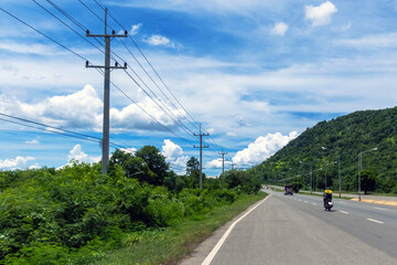 Beautiful view of asphalt highway road with electric pole and green mountain with sky clouds. Landscape with curved roadway through mountain pass in spring. Journey in nature mountain road. Travel.
