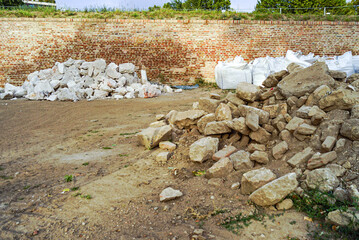 A pile of stones and sacks of building material against the backdrop of a defensive brick wall -...