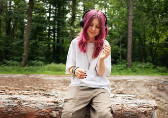 Young relaxed girl listening music with headphones in forest