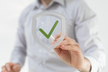 Image of a person drawing a checkmark inside a shield, symbolizing security and protection.