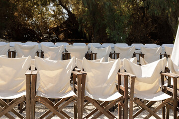 Rows of white canvas folding chairs outdoors under trees. Perfect for event, theater, or summer...