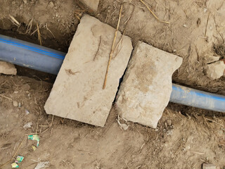 Rural irrigation pipeline covered with planks on mud road near farmland, allowing pedestrian...