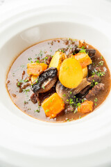 Hearty vegetable stew with mushrooms, potatoes, and herbs served in a white bowl on a light...