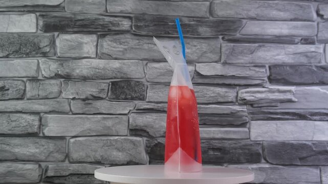 Adult drink in reusable pouch with drinking straw, rotating. Alcohol cocktail in plastic bag very convenient for picnics and gatherings. Red drink or fruit fermenting beverage.