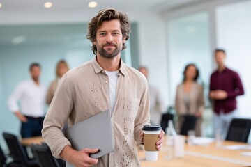 Confident young professional holding laptop and coffee before morning meeting, casual dress code in creative office environment
