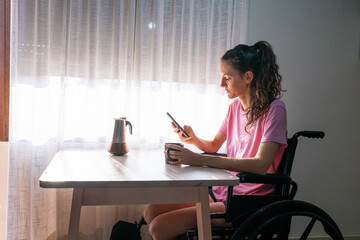 Woman with disability using mobile phone and drinking coffee at home