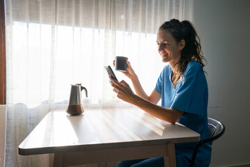 Nurse drinking coffee and browsing smartphone at home