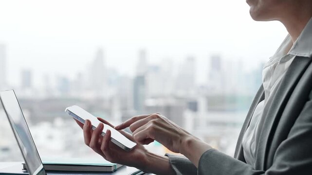 都市のオフィスビルでノートパソコンとスマホを使って作業する女性ビジネスパーソン