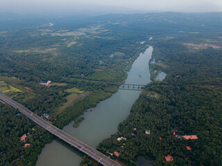 Aerial view of a verdant landscape where the Talpona River carves a path through dense forests, crossed by bridges under a vast sky, Canacona, Goa, India.