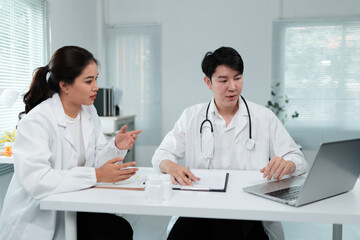 Two asian doctors wearing lab coats are discussing a diagnosis using a laptop computer in a bright...