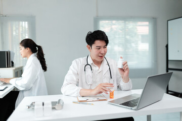 Fototapeta premium Asian doctor holding bottle of pills and explaining treatment during online consultation with patient using laptop in hospital