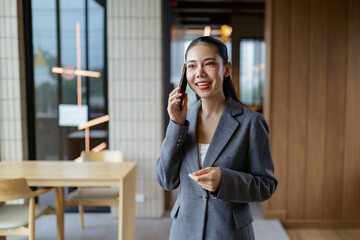 Smiling Asian businesswoman engaging in a conversation on her mobile phone while seated in a modern...