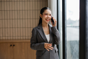 Young manager wearing suit using smartphone having conversation and smiling near window in office