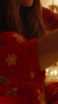 Vertical video. Young Woman in Santa Hat Wrapping Lights Around Small Christmas Tree in Warmly Lit Room, Close Up Side Angle, Dolly Slider Movement
