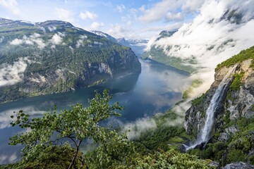 Gjerdefossen waterfall, at Ørnesvingen viewpoint, atmospheric clouds over the fjord in the morning light, at Geirangerfjord, near Geiranger, Møre og Romsdal, Norway