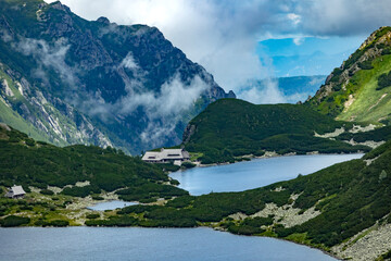 Mountain lake with alpine huts surrounded by green slopes and misty rocky peaks