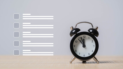 A classic black alarm clock sits on a wooden surface next to a graphic checklist with empty boxes and horizontal lines.