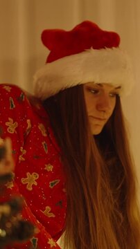 Vertical video. Close Up of Woman in Santa Hat Looking Toward Decorated Tree with Warm Light in Background and Festive Mood