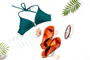 Stylish bikini swimsuit with sandals and tropical leaves, top view. Vacation beach accessories