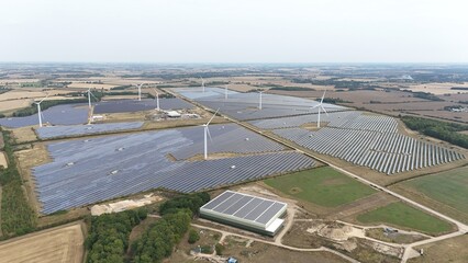Aerial drone shot of wind turbine and solar panel photovoltaic power plant, generating renewable energy electricity in England UK © Liam Carter