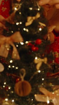 Vertical video. Close Up of Woman Decorating Mini Christmas Tree with Ornaments While Sitting on Carpet in Cozy Room