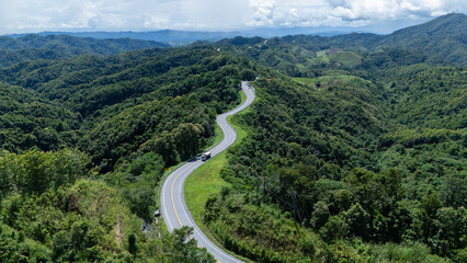 A scenic view of a winding road through lush green mountains under a partly cloudy sky, showcasing the beauty of nature.