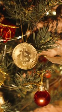 Vertical video. Golden Bitcoin Coin Hanging on Christmas Tree Surrounded by Lights Berries and Ornaments with Warm Lighting Suggesting Crypto Holiday Investment