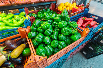 A high-angle view displays a plentiful heap of vibrant green bell peppers overflowing from an...
