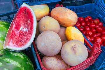 Colorful fresh produce in blue plastic shopping baskets featuring sliced watermelon, cantaloupe...