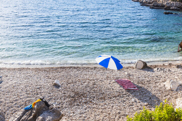 Peaceful Mediterranean beach scene with classic blue and white umbrella on pristine pebble shore...