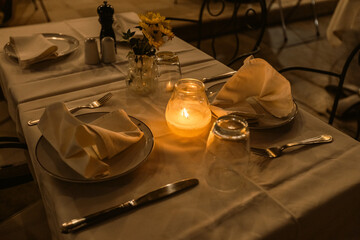 Intimate restaurant table beautifully set with glowing candles, yellow sunflowers, and elegant place settings creating perfect romantic dining atmosphere.