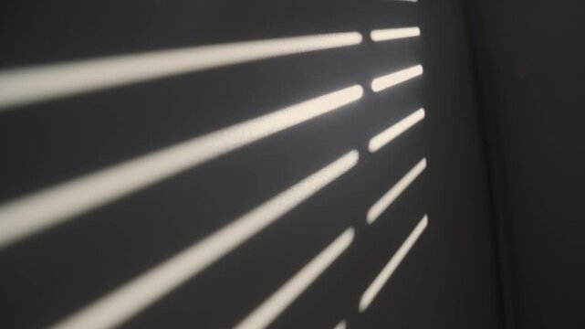 Sunlight casting shadows from window blinds opening onto a dark wall, creating a dynamic abstract pattern of light and shadow, representing awakening new beginnings and the passage of time