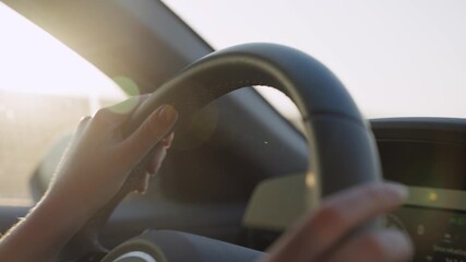 Female hands on car steering wheel driving on highway road with sun shining. Close up on wheel as woman holding it commuting to work or going on vacation or escaping. Sunset or sunrise in background - Powered by Adobe