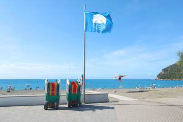 Blue flag on beach by sea. Nature and ecology, sky. Mountains and landscape of Liguria, Italy.