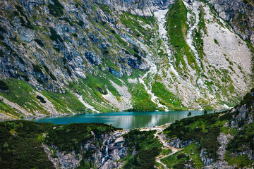 Mountain lake at the base of steep rocky slopes with green patches and a small waterfall