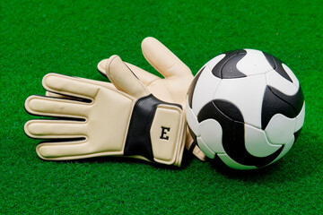 Soccer goalkeeper gloves lying on artificial grass next to soccer ball, showcasing essential sports equipment for football training or match preparation, no people visible