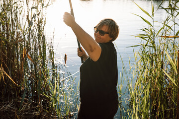 Happy mature woman fishing with a small fish caught on the hook during a sunny day. A person...